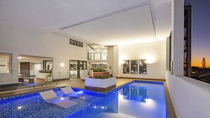 A modern indoor pool area with clear blue water, lounge chairs, and a well-lit interior. - Hedge Apartments by CLLIX (Buddina)