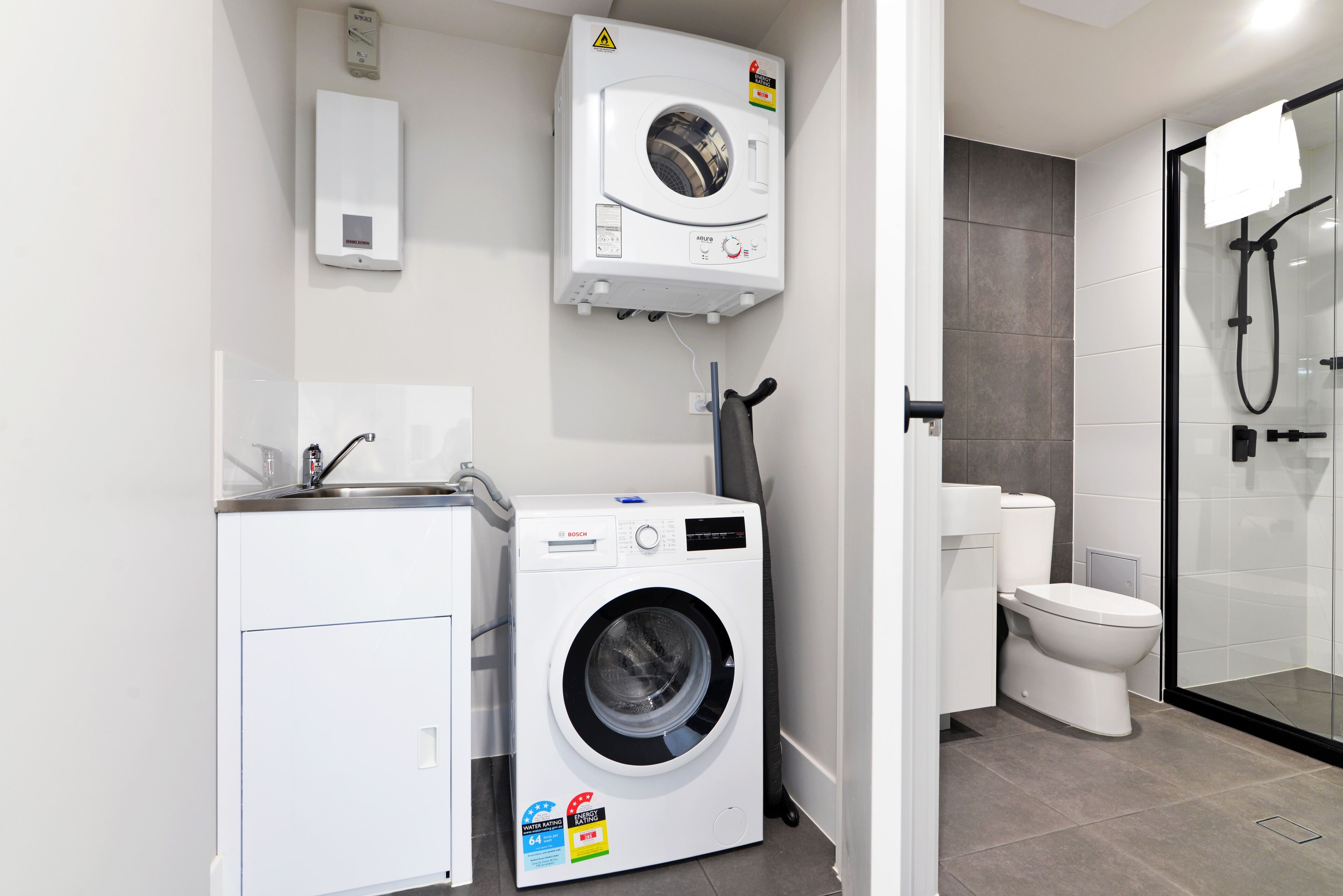 Ein kleines Badezimmer mit Waschmaschine, Toilette und Duschkabine aus Glas.