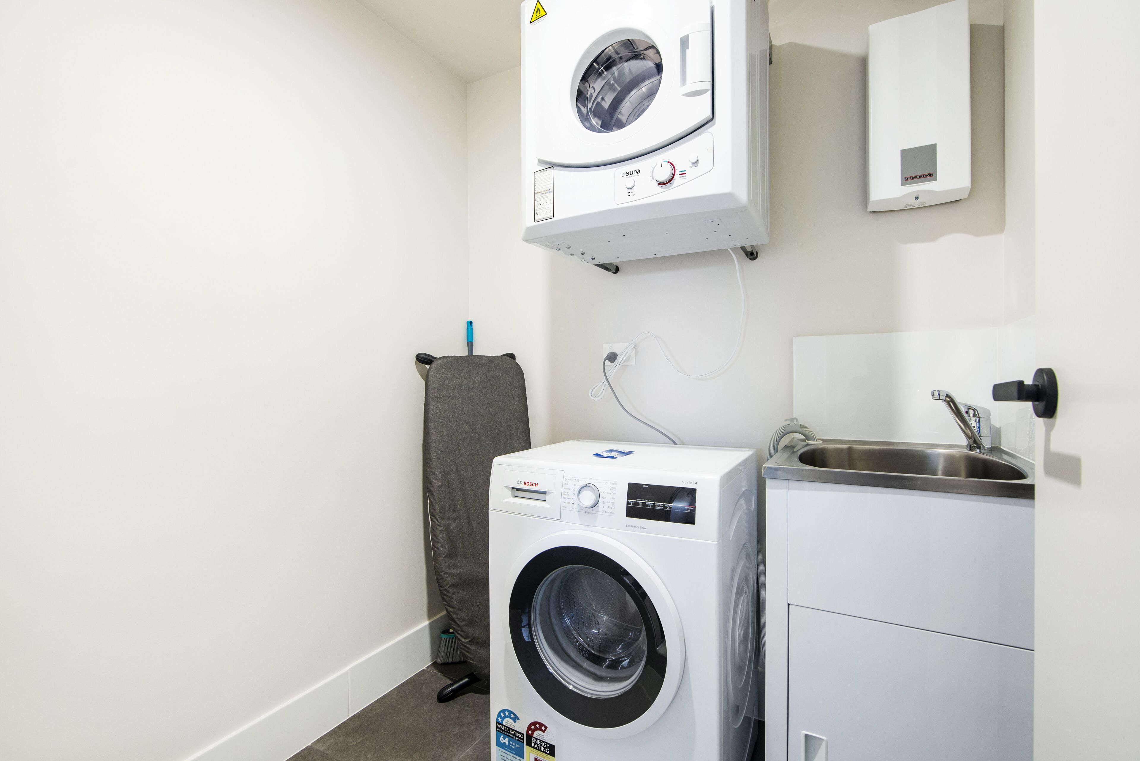 A compact laundry area with a front-loading washing machine, a wall-mounted dryer, and a small sink.