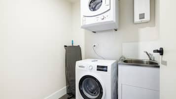 A compact laundry area with a front-loading washing machine, a wall-mounted dryer, and a small sink.