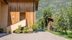 A wooden building with a staircase leading to an entrance, surrounded by greenery and a mountainous backdrop.