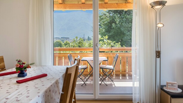 A room with a balcony, a table with chairs, a vase of flowers, and a lamp.
