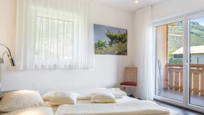 Een slaapkamer met een bed, een stoel, een schilderij en uitzicht op een balkon.