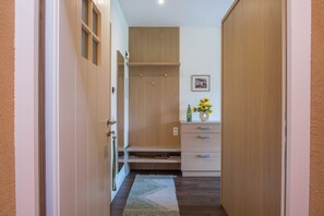 Um corredor com portas de madeira, uma pequena prateleira com um vaso de flores e um quadro na parede.