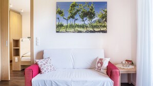 Een slaapkamer met een bed, nachtkastje, raam en een schilderij van bomen aan de muur.