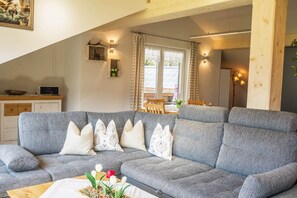 A modern living room with a grey sofa, decorative pillows, a wooden coffee table, and a dining area in the background.