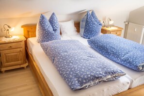 A bed with blue floral bedding, wooden headboard, bedside tables with lamps, and a wooden floor.