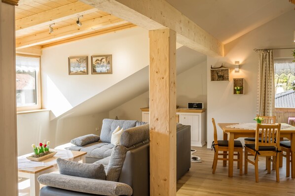 A cozy living area with a sofa, a dining table with chairs, a staircase, and a kitchen area.