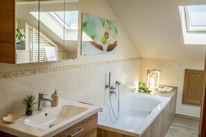 A modern bathroom with a skylight, a large bathtub, a sink, and a mirror.