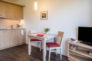 Een moderne keuken met houten kasten, een eettafel met rode kussens, een potplant en een tv op een meubel.