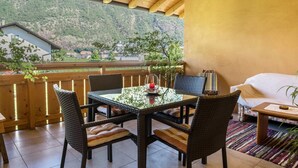 A covered outdoor dining area with a table and chairs, a sofa, and a view of a mountainous landscape. - Apartment “Urbanhof - Moritzing” with Mountain View, Wi-Fi & 2 Balconies (Bozen)