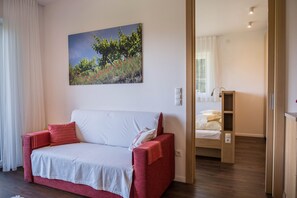 Een kamer met een rode bank, een bed, een schilderij van bomen en bloemen, en een houten vloer.