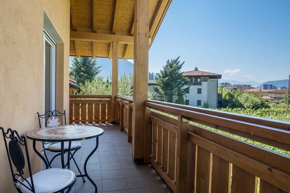 Un balcón con baranda de madera, una mesa con sillas y vistas a edificios y árboles.