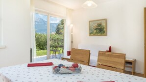 Une chambre à coucher comprenant un lit, une table de chevet, une lampe et une fenêtre donnant sur un paysage verdoyant et des montagnes.