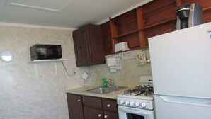 A compact kitchen with a white refrigerator, a stove, and a microwave. There is a small sink and a window above the sink. - Romatic Retreat at the Honeymoon Sunday Cottage located at the Oceana Cottages (North Truro)