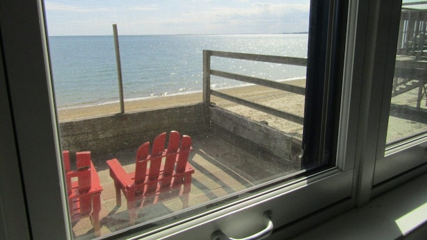 A window with a view of a beach and red chairs outside. - Romatic Retreat at the Honeymoon Sunday Cottage located at the Oceana Cottages (North Truro)