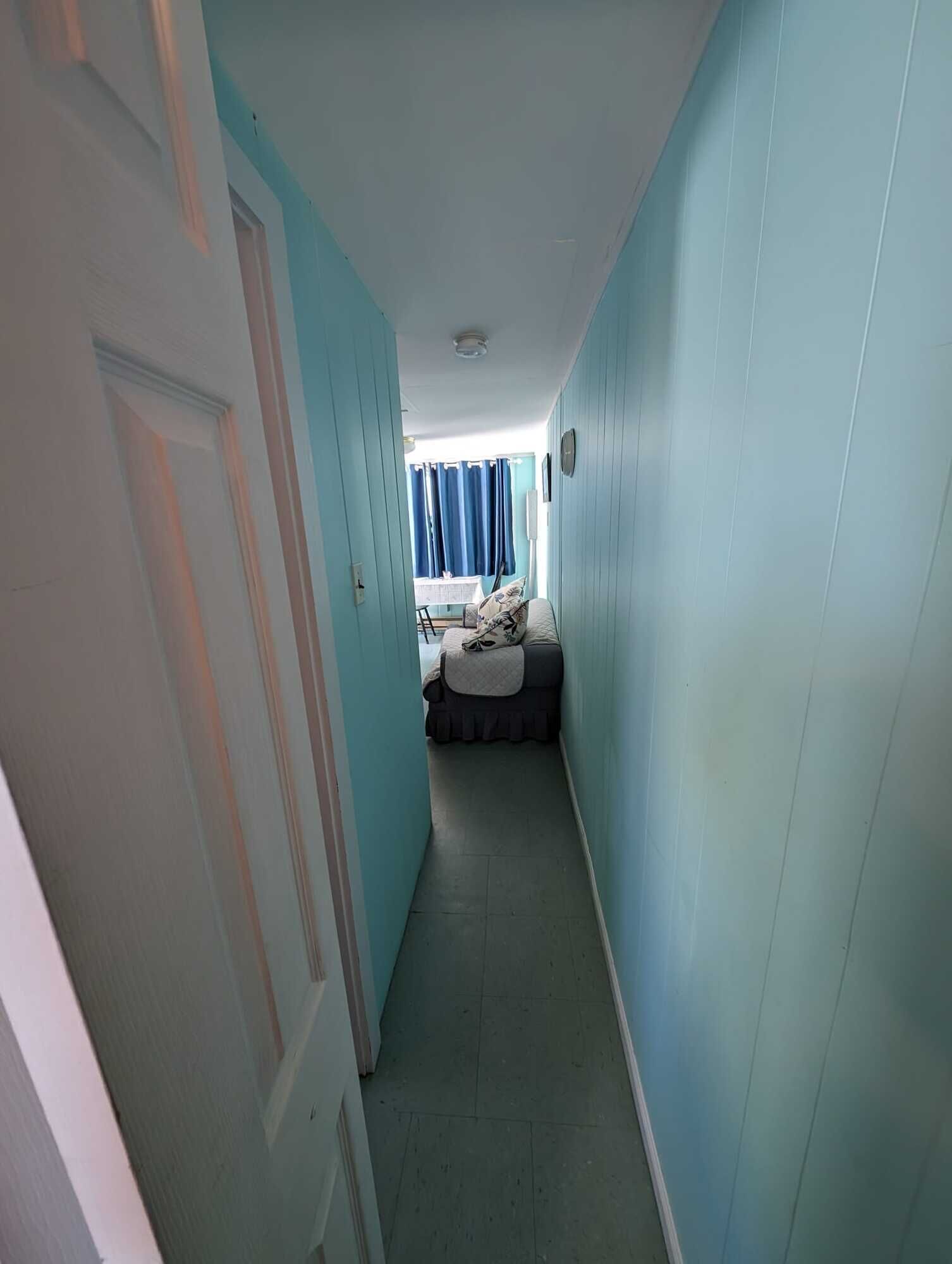 Un pasillo estrecho con paredes azul claro y una puerta a la izquierda.