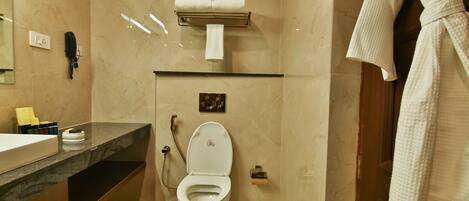A modern bathroom with a marble floor, a white toilet, a towel rack, and a robe hanging on the door.