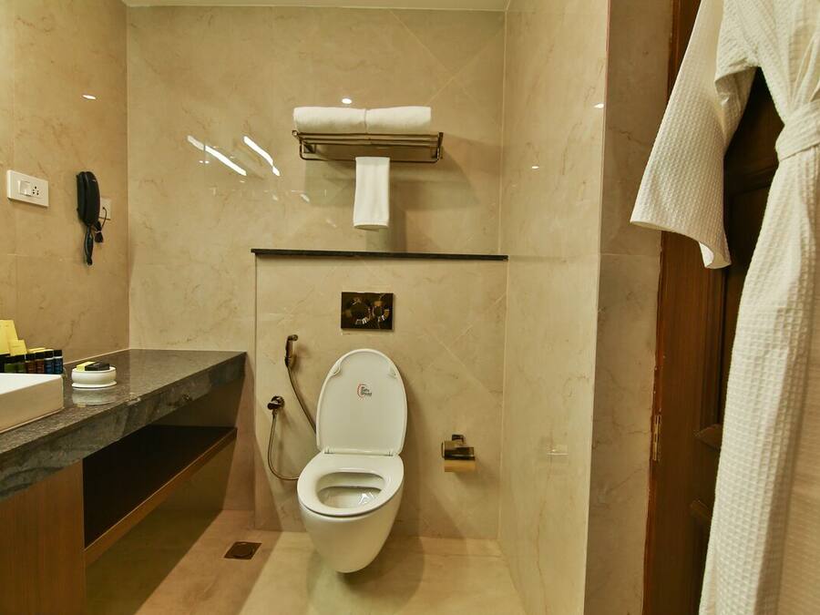 A modern bathroom with a marble floor, a white toilet, a towel rack, and a robe hanging on the door.