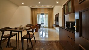 A modern hotel room with a dining area, a sofa, a TV, and a kitchen area. - Accord Chrome (Chennai)