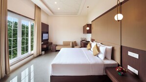 A hotel room with a large bed, a TV, a desk, and a view of greenery through the window. - Accord Chrome (Chennai)
