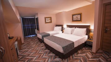 A hotel room with two beds, a wooden wardrobe, a desk with a chair, and a herringbone-patterned floor.