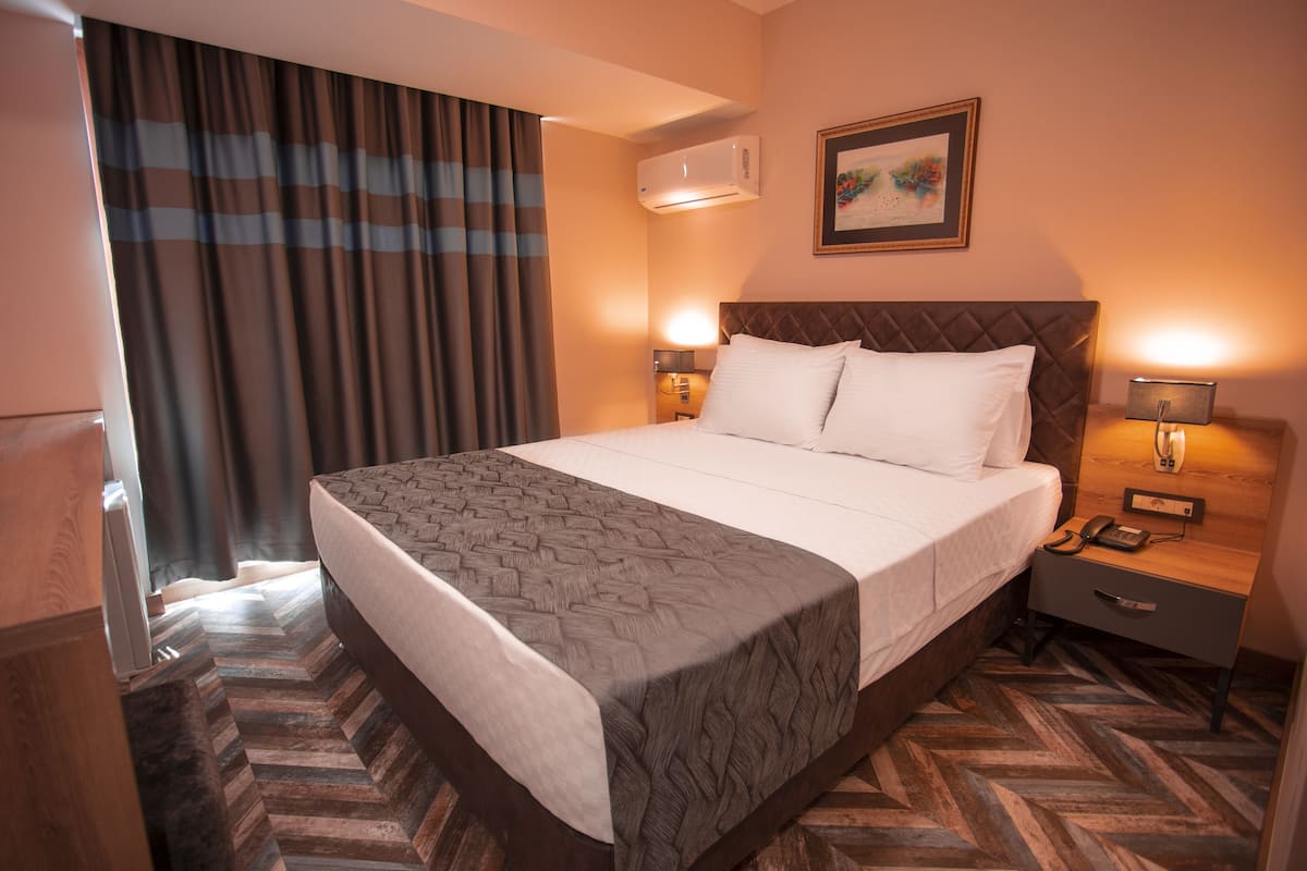 Habitación de hotel con una cama grande, una mesita de noche con lámpara, teléfono y aire acondicionado instalado en la pared.