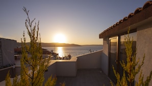 A balcony with a view of the sea at sunset, a building with a tiled roof, and some greenery in the foreground. - Hotel Kale 17 (Çanakkale)