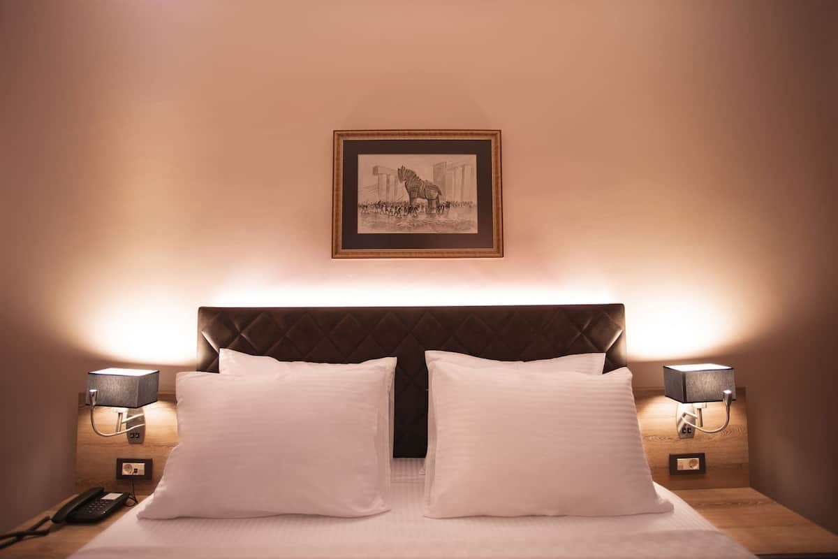 Habitación de hotel con cama, dos lámparas de noche, un cuadro en la pared y un teléfono en la mesita de noche.