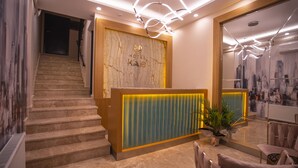A hotel reception area with a marble staircase, a reception desk with a cityscape mural, and a seating area with a plant. - Hotel Kale 17 (Çanakkale)