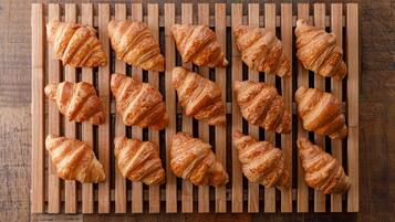 A wooden board with multiple croissants arranged in rows.