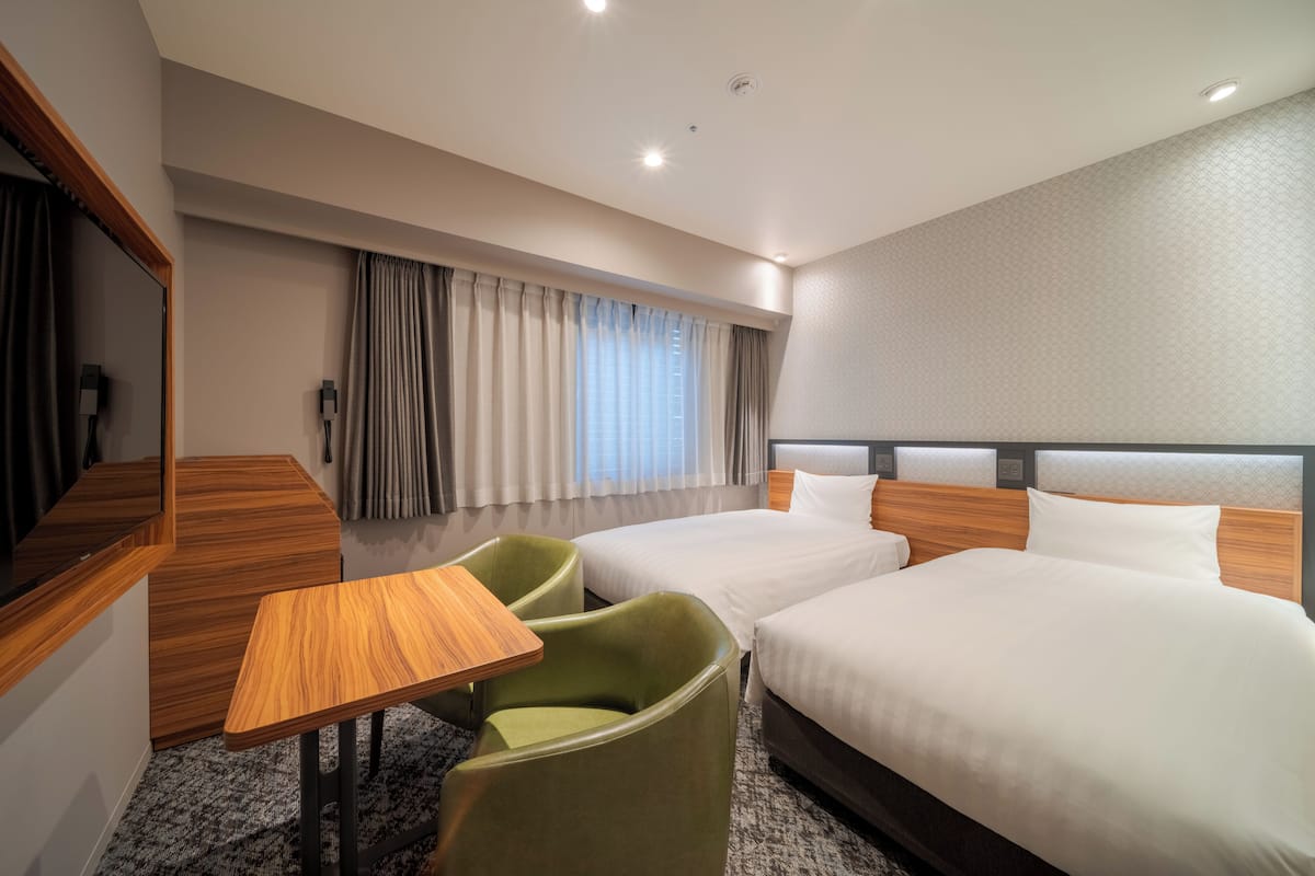 A hotel room with two beds, a desk, a chair, and a large window with curtains.