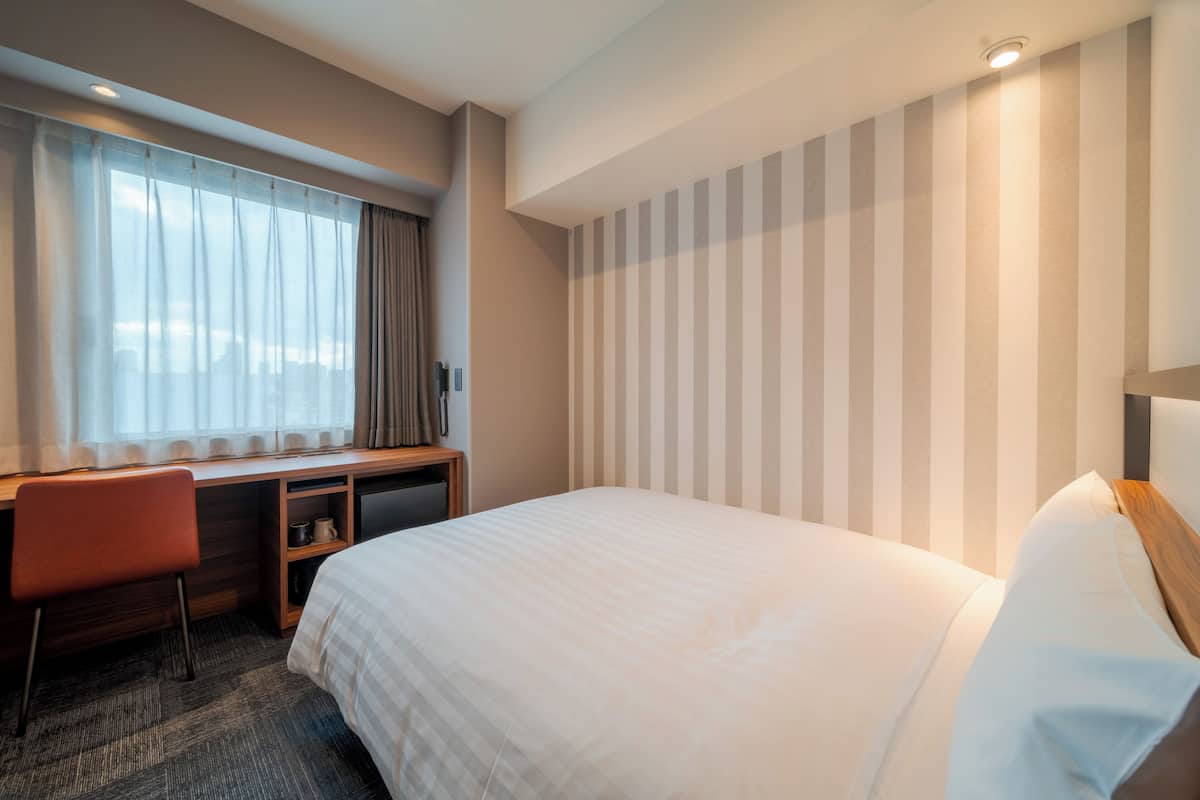 A hotel room with a bed, a desk, a chair, and a window with curtains.