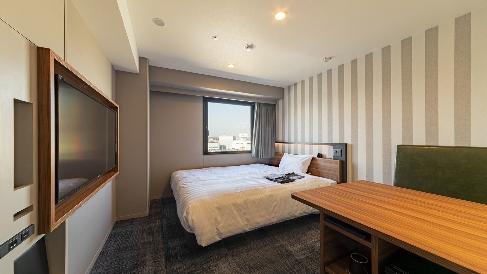 A hotel room with a bed, a desk, a television, and a window with a city view.