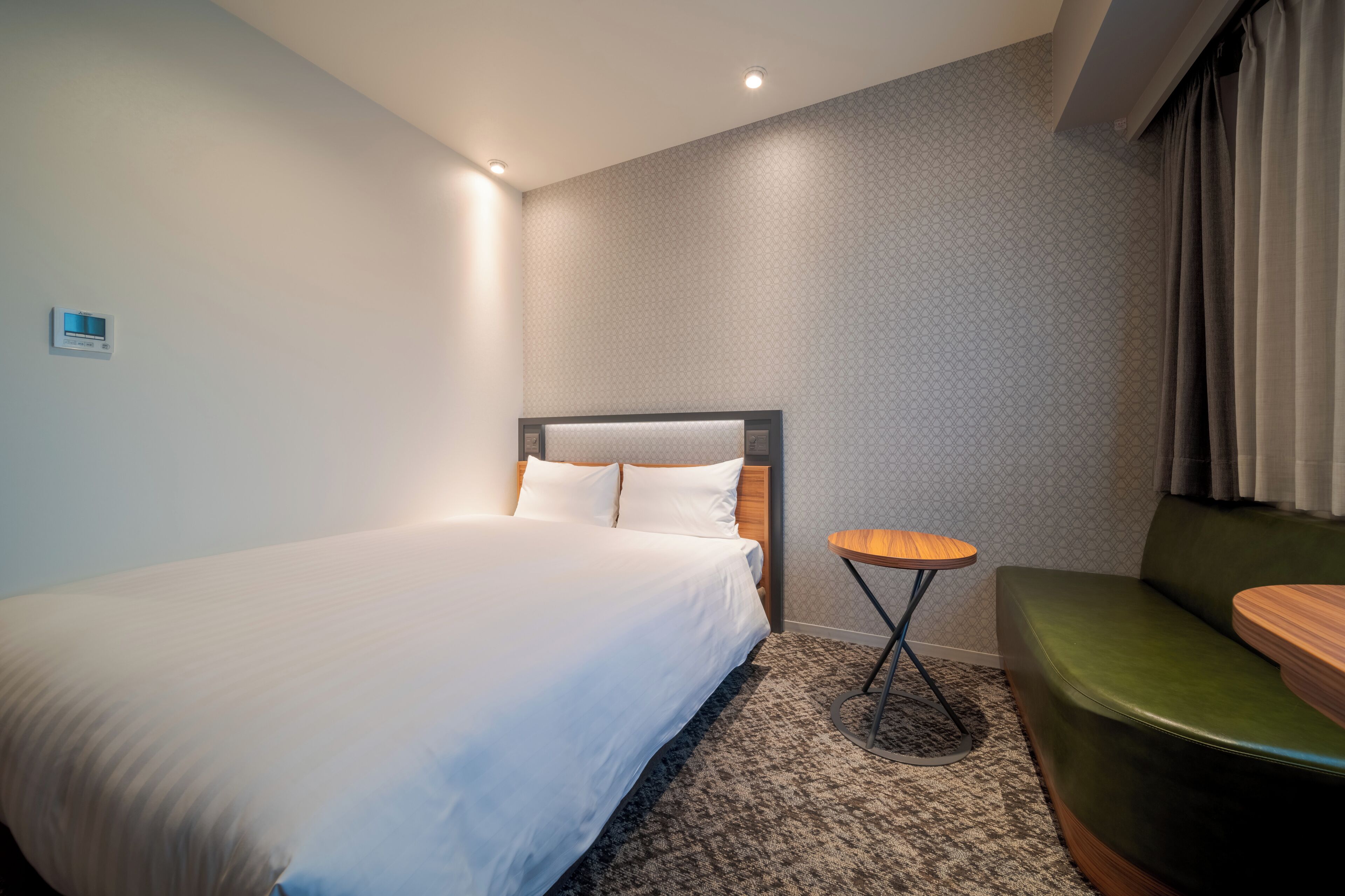 Ein Hotelzimmer mit einem großen Bett, einem kleinen runden Tisch, einer grünen Couch und einer Wand mit Muster.