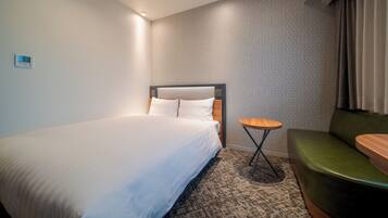 Ein Hotelzimmer mit einem großen Bett, einem kleinen runden Tisch, einer grünen Couch und einer Wand mit Muster.