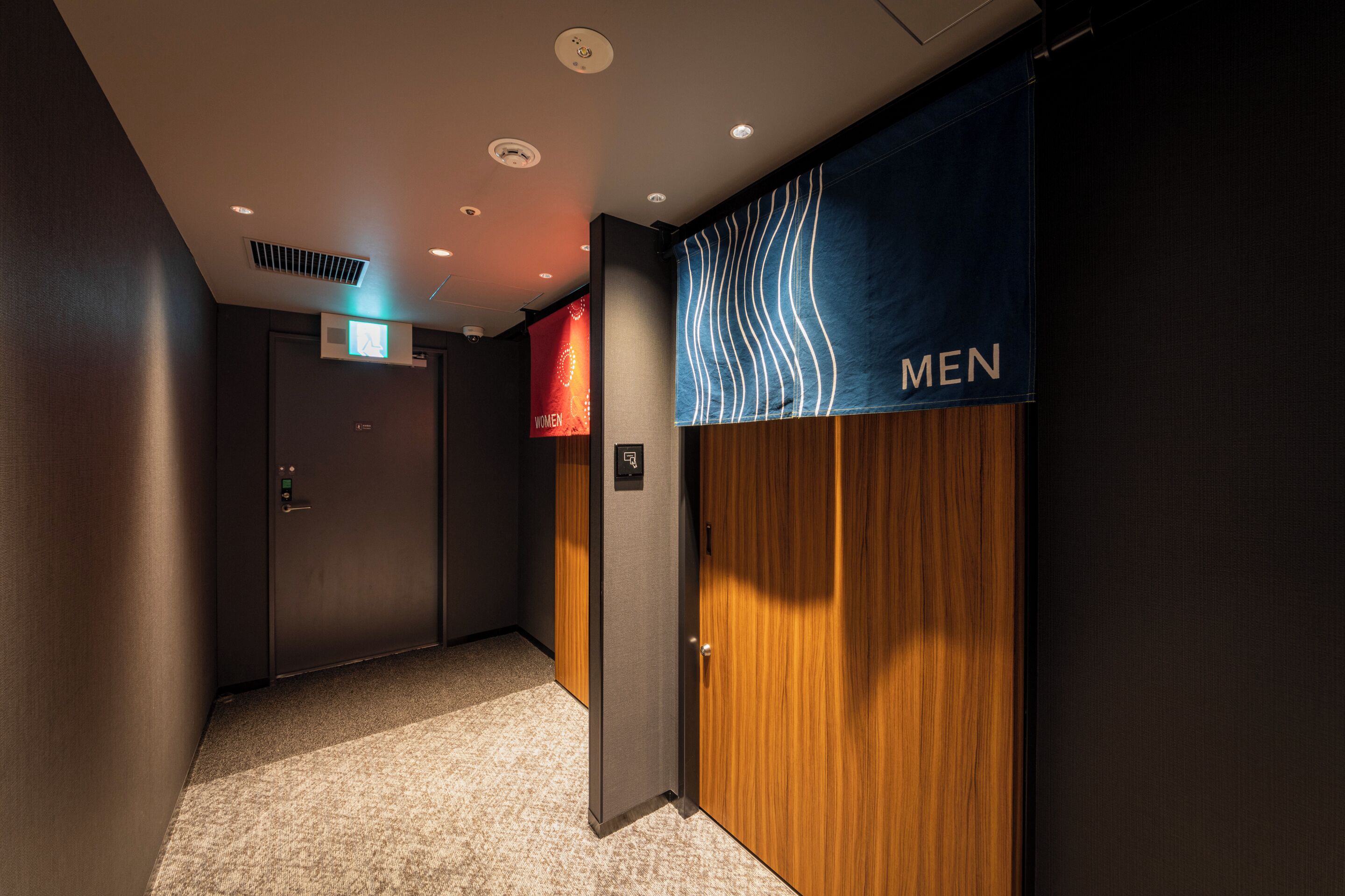 A hallway with a men's restroom sign, a door with a digital display, and a carpeted floor.