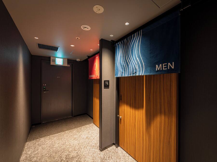 A hallway with a men's restroom sign, a door with a digital display, and a carpeted floor.