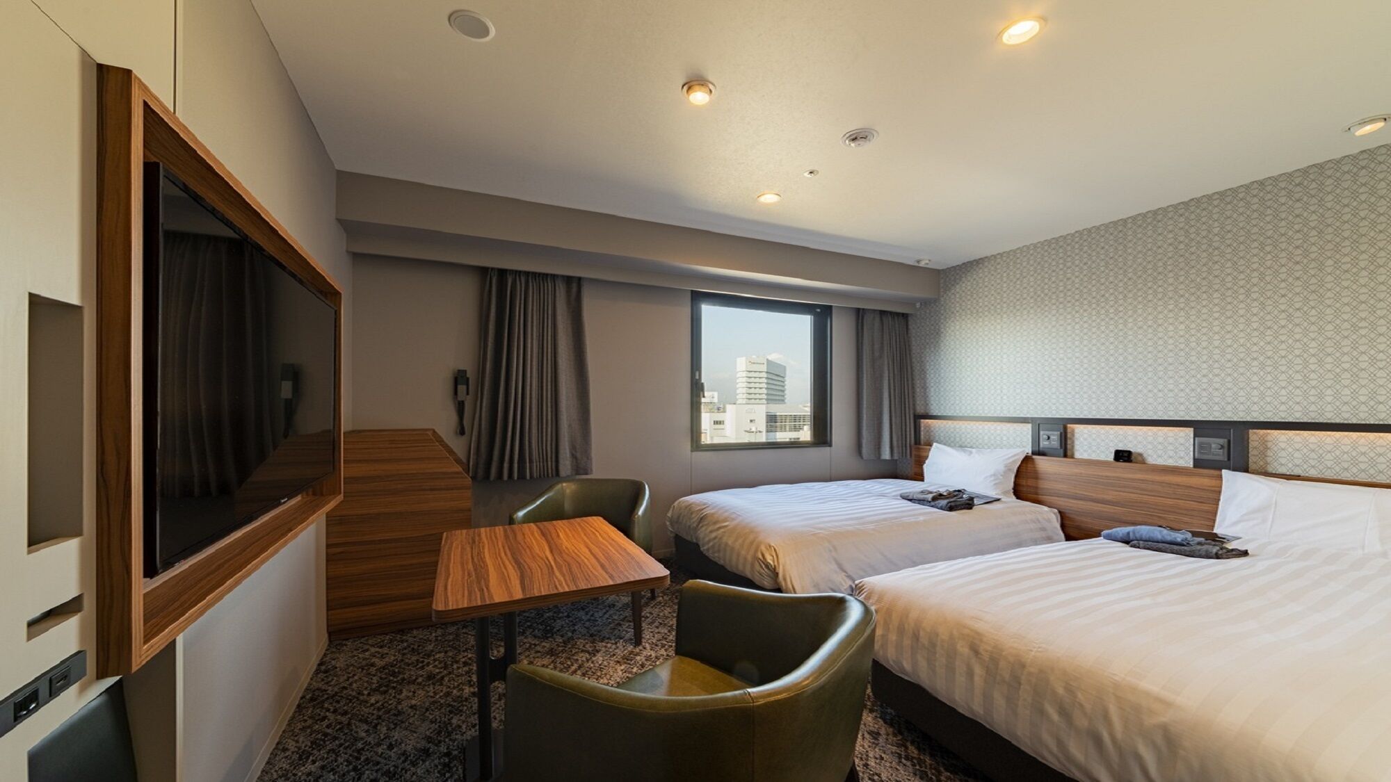 A hotel room with two beds, a desk, a chair, a TV, and a city view.