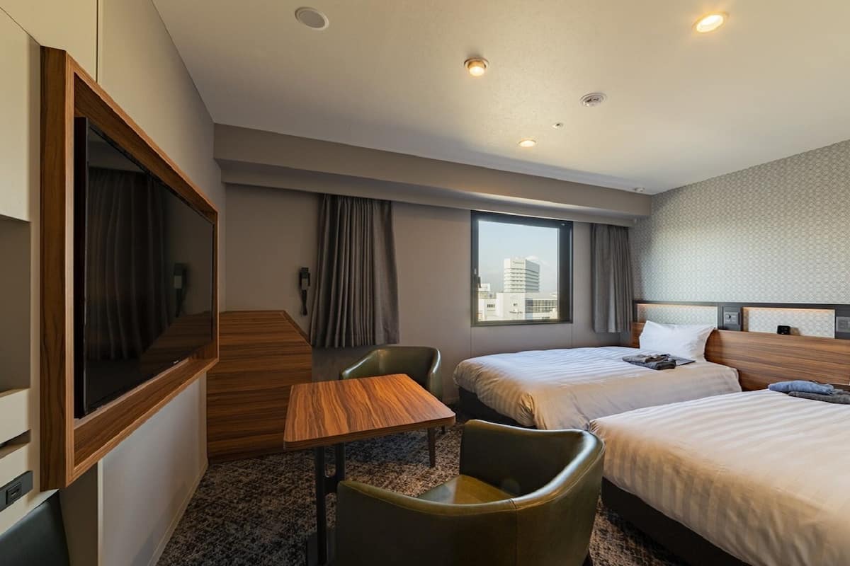 A hotel room with two beds, a desk, a chair, a TV, and a city view.
