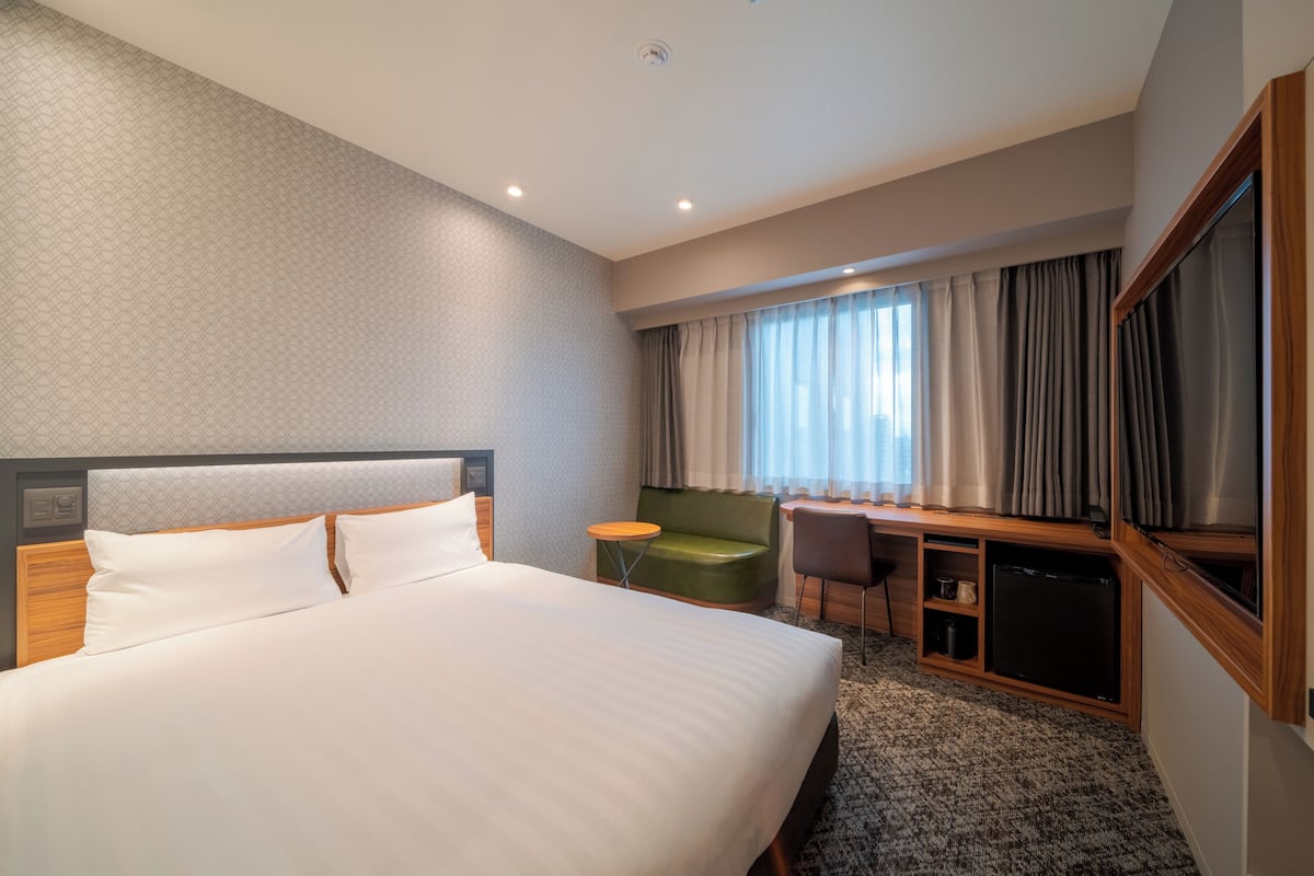 A hotel room with a large bed, a desk, a chair, a television, and a small table.