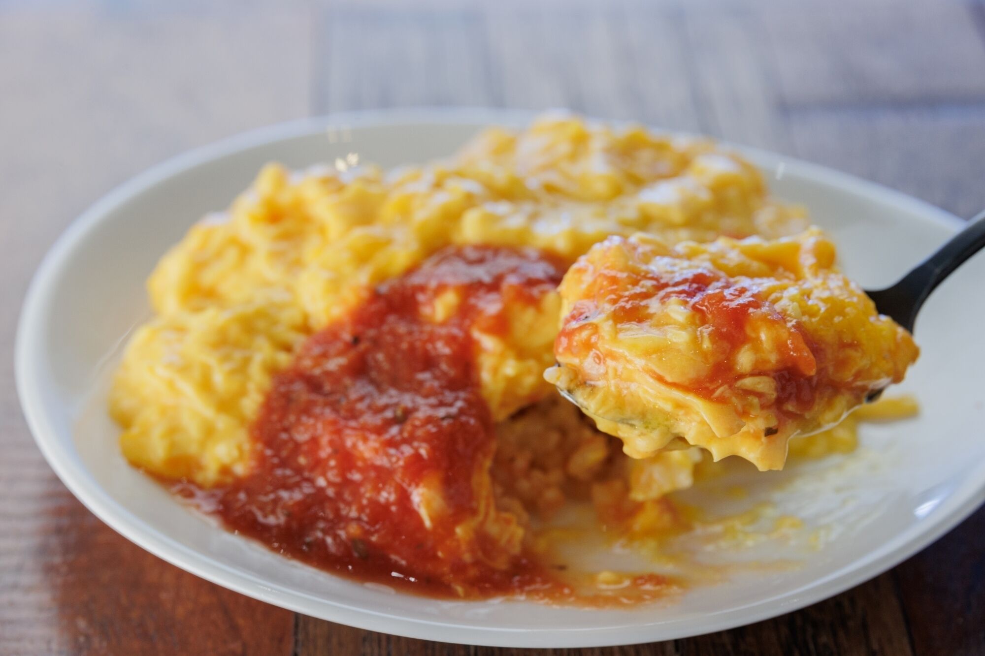 A plate of scrambled eggs with a spoonful of tomato sauce.