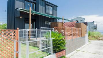 A modern two-story house with a balcony, a fenced garden area, and a view of the sea.
