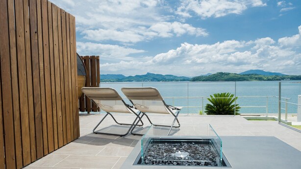 Une terrasse avec deux fauteuils, une table à plateau en verre et un foyer extérieur.