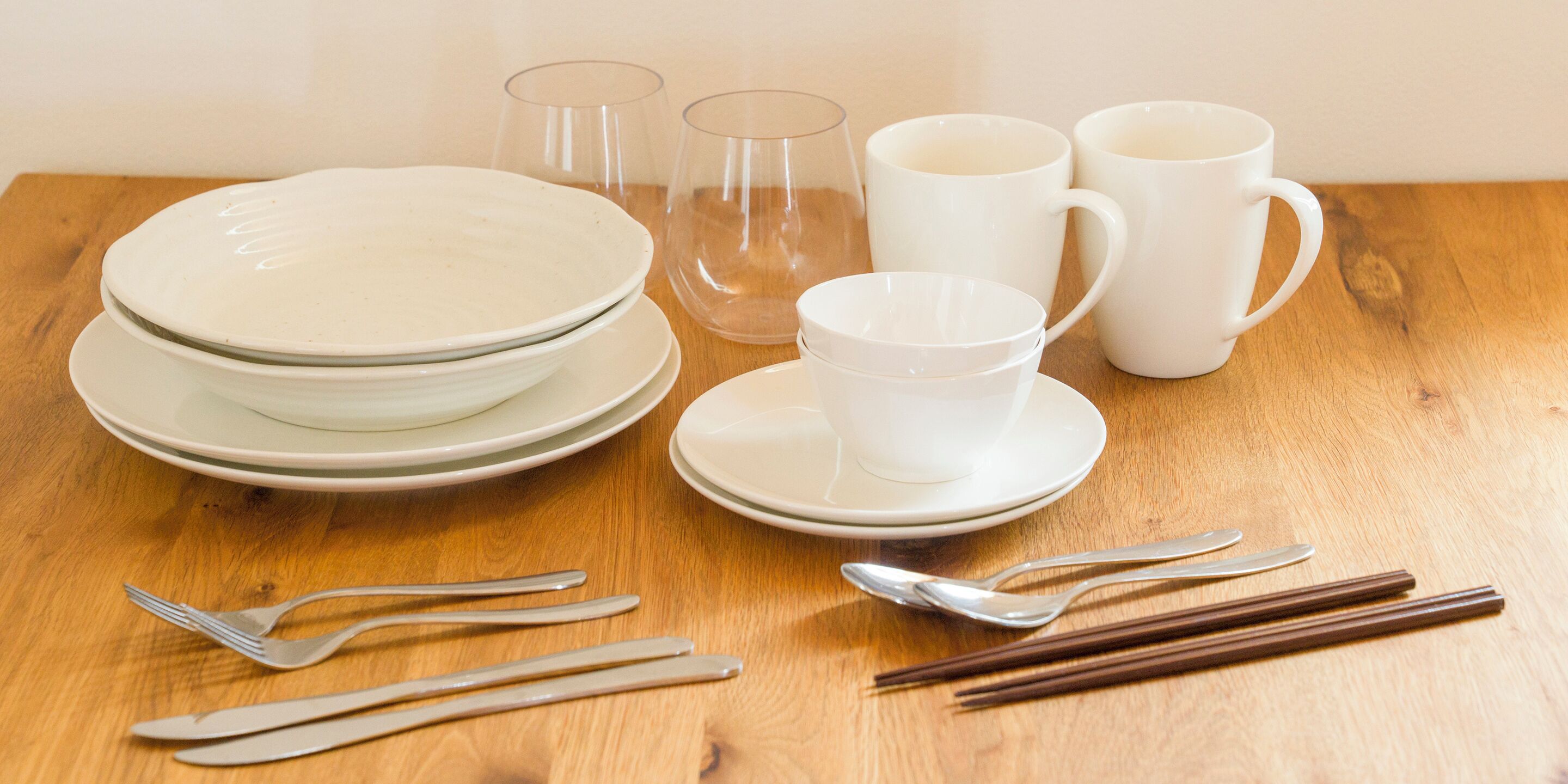 A wooden table with white plates, cups, glasses, and cutlery.