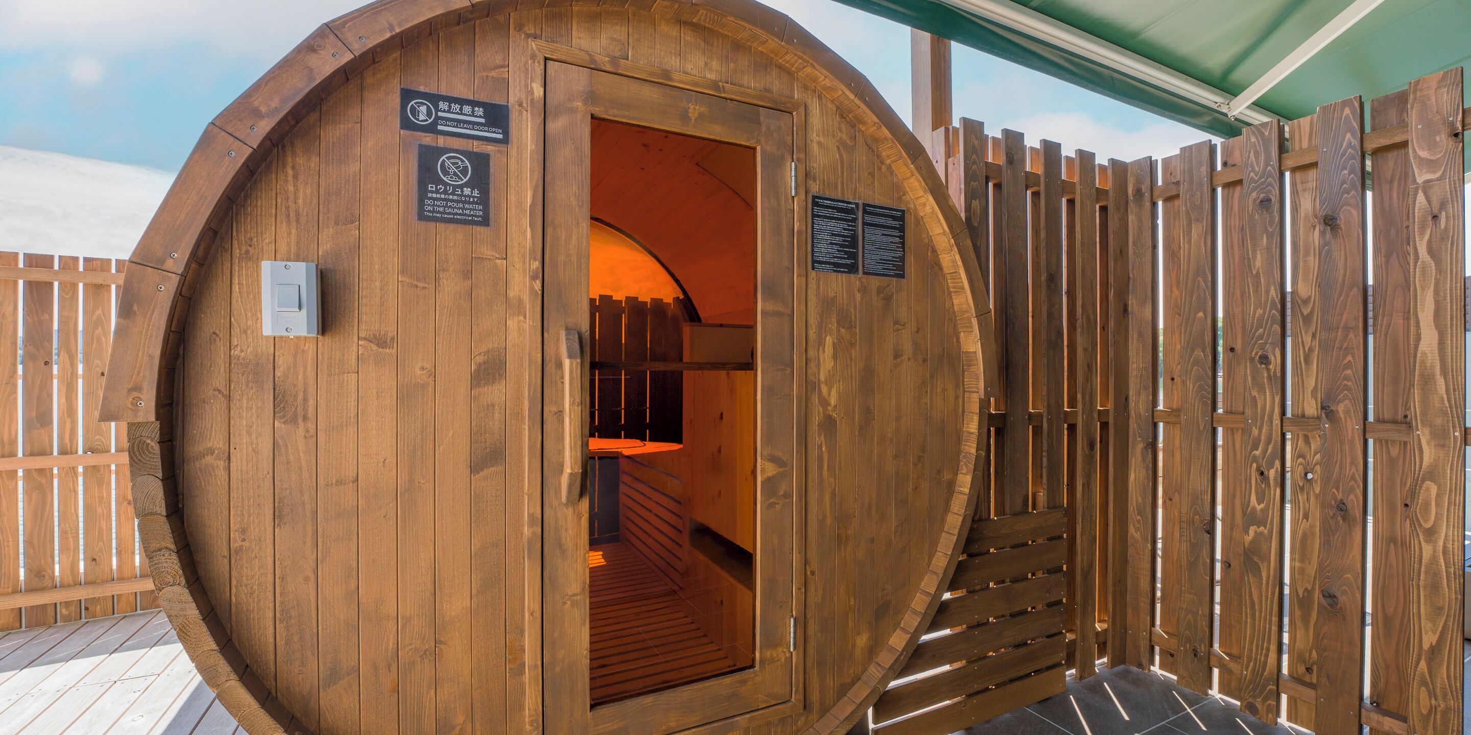 Una sauna de madera con puerta, valla de madera y terraza de madera.
