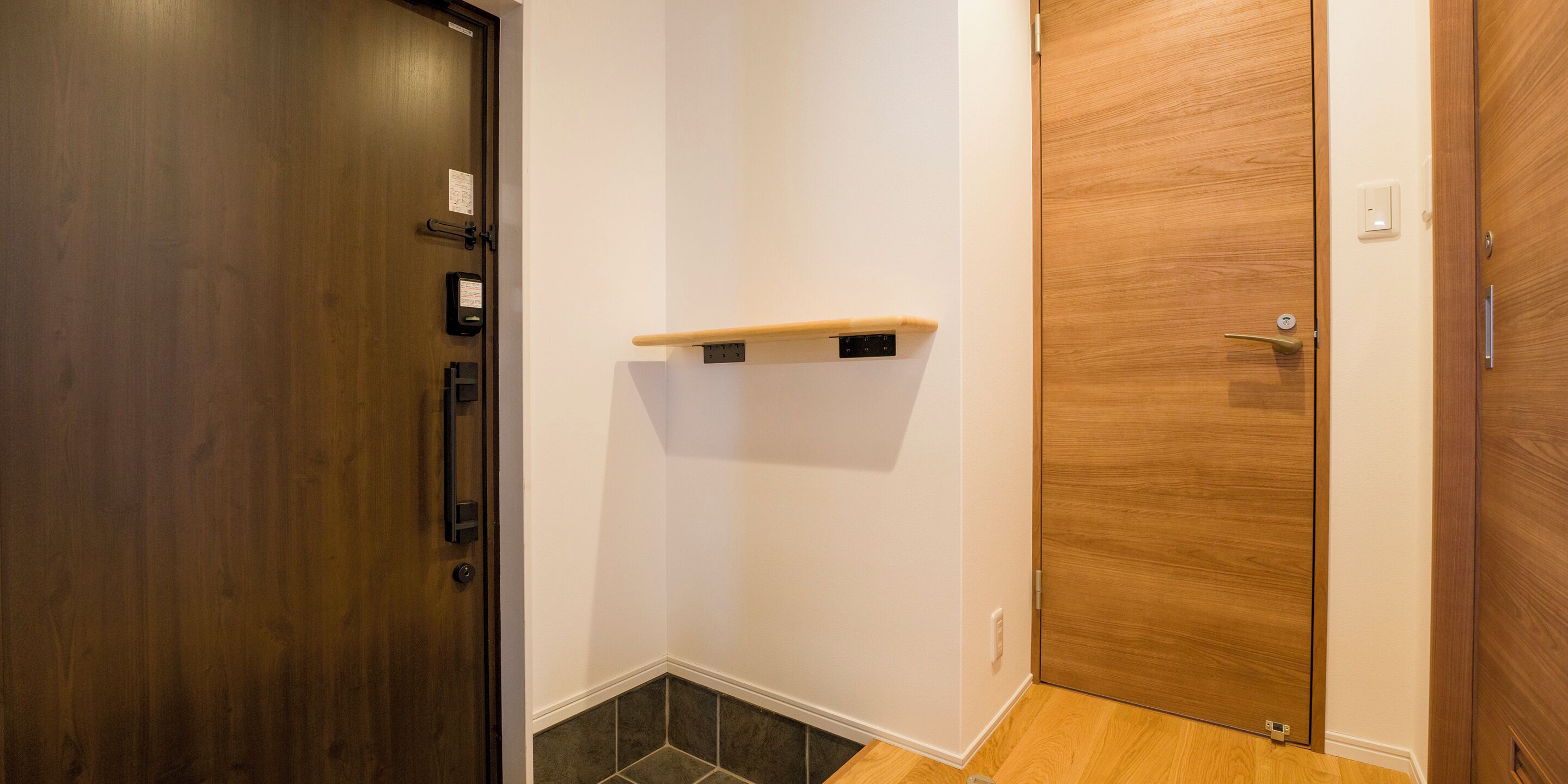 A hallway with a wooden door on the left, a wooden door on the right, and a small shelf mounted on the wall.
