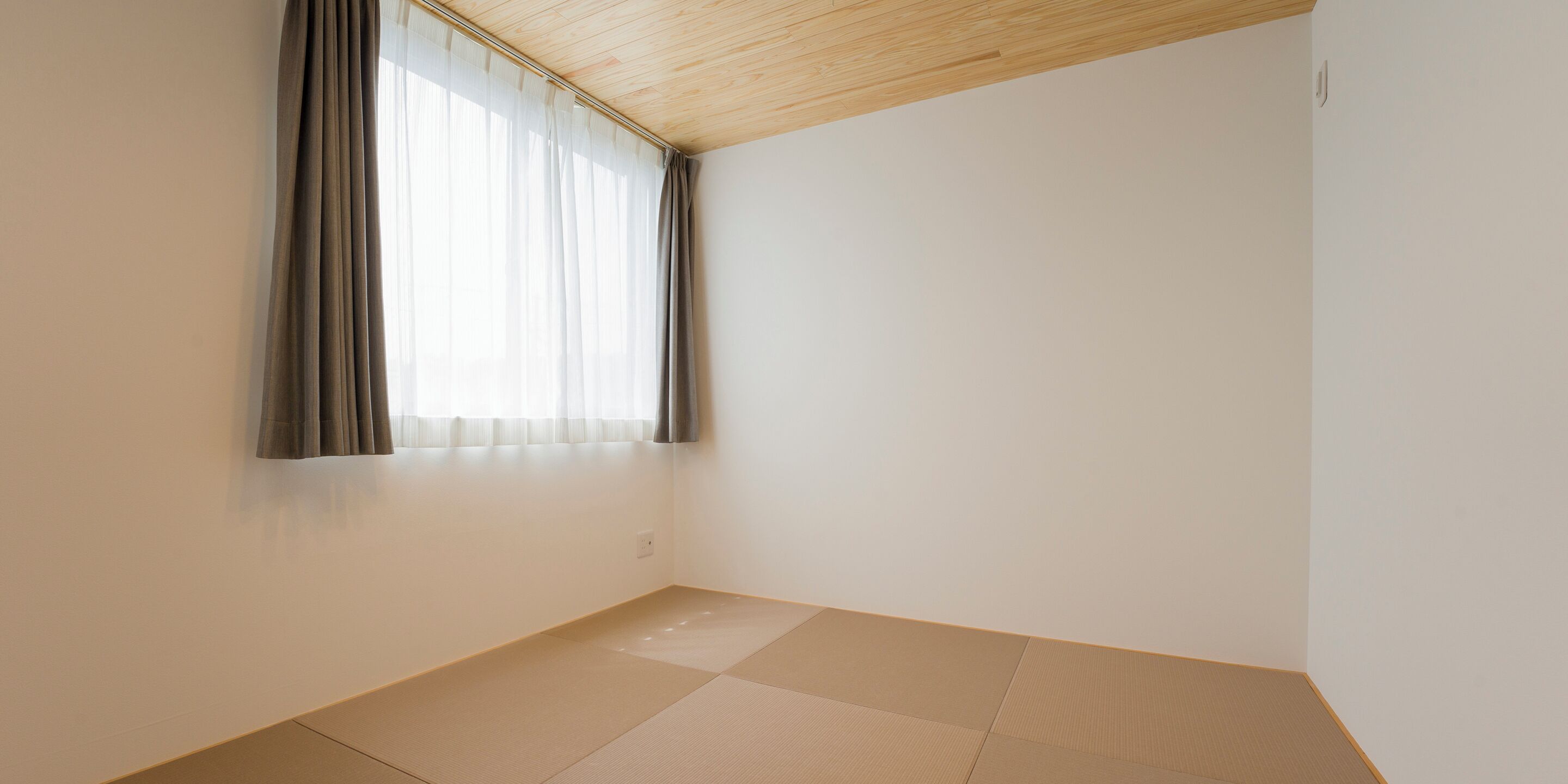 Una habitación con techo de madera, una ventana con cortinas traslúcidas y suelo de esteras de tatami.