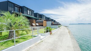 Un hĂŽtel situĂ© au bord de lâeau, dotĂ© dâune architecture moderne, dâune promenade en bĂ©ton et offrant une vue sur la mer.