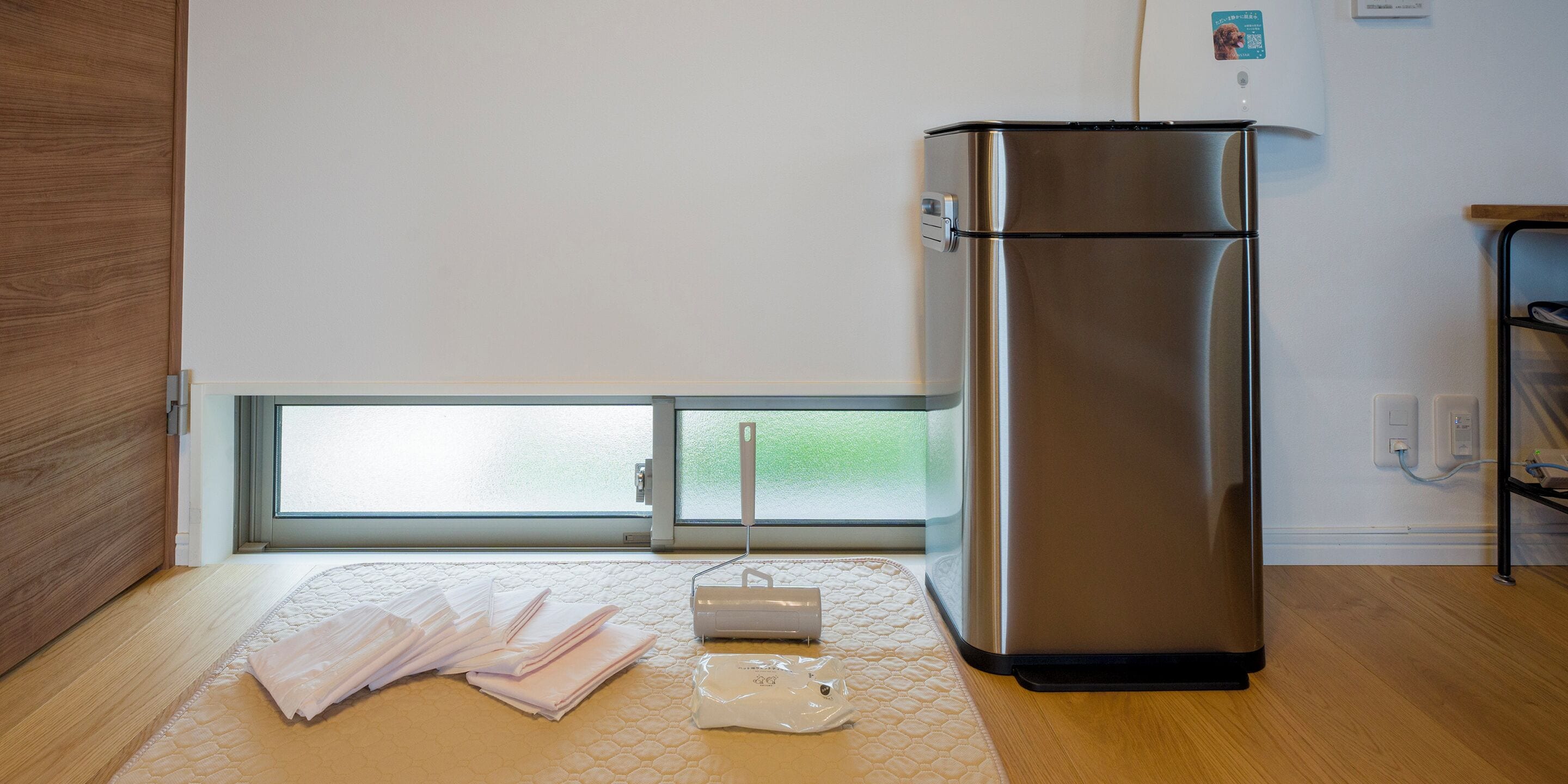 A modern kitchen with a stainless steel refrigerator, a wooden floor, and a window with a view of greenery.